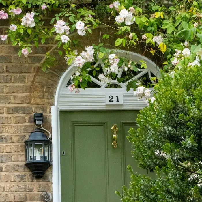 A green panelled front door with a fanlight, framed by climbing roses