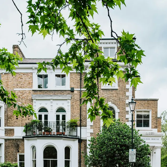 A large Victorian villa with white bay windows and a balcony, behind a hedge