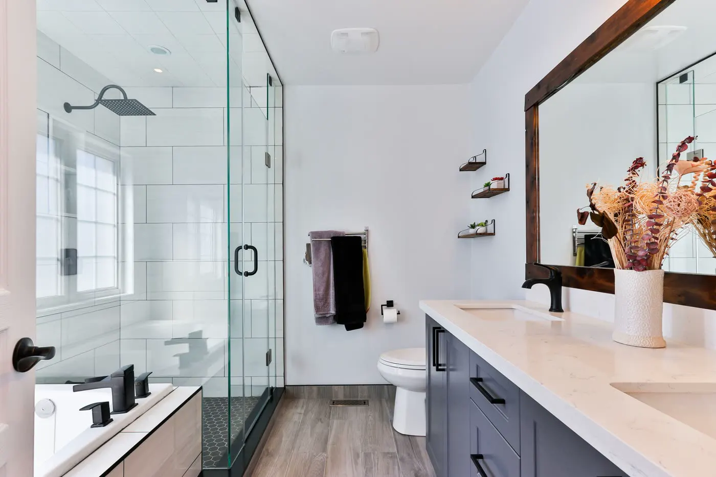A bathroom with a glass walk-in shower, double vanity and wood-effect floor