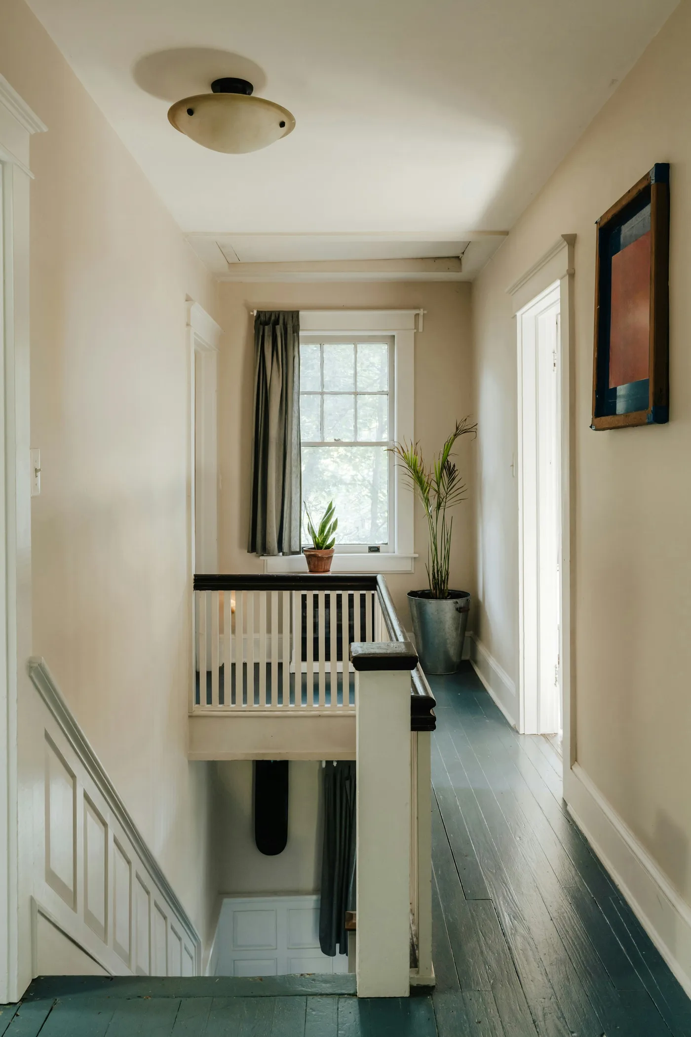 An upstairs landing with painted floorboards, a panelled staircase and a sash window